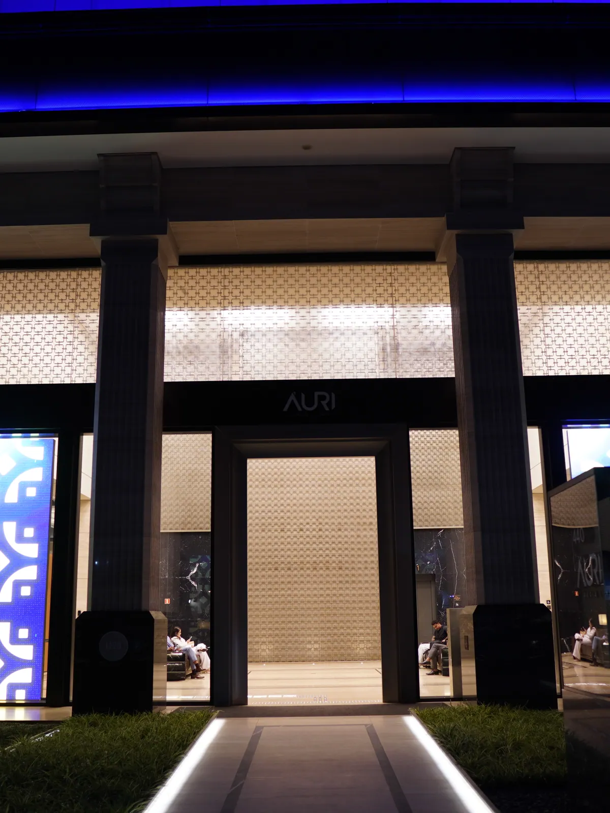 Entrada principal do edifício à noite, com totens iluminados